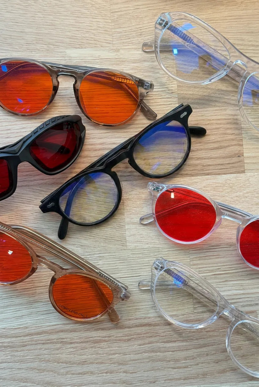 Assortment of blue light glasses with red, orange, and clear lenses on a wood surface