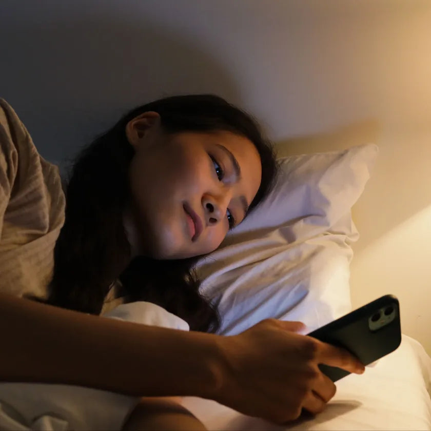 Woman lying in bed using a smartphone in a dimly lit room
