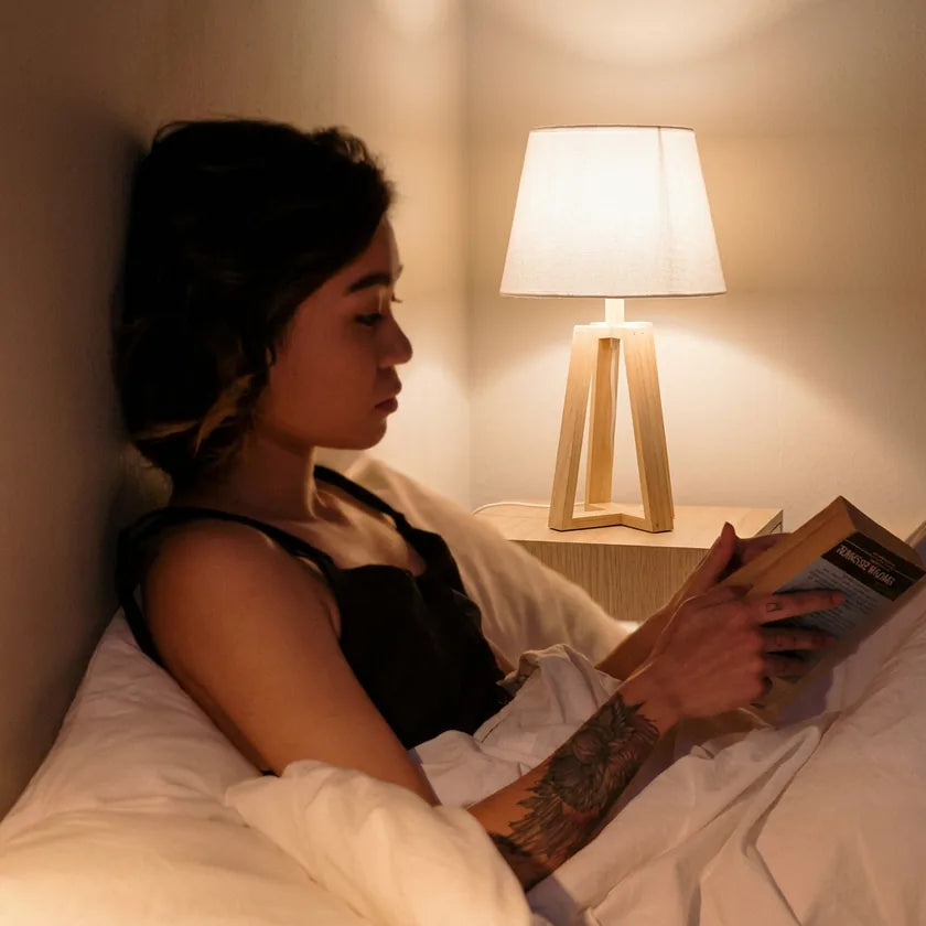 Woman reading a book in bed under a warm lamp